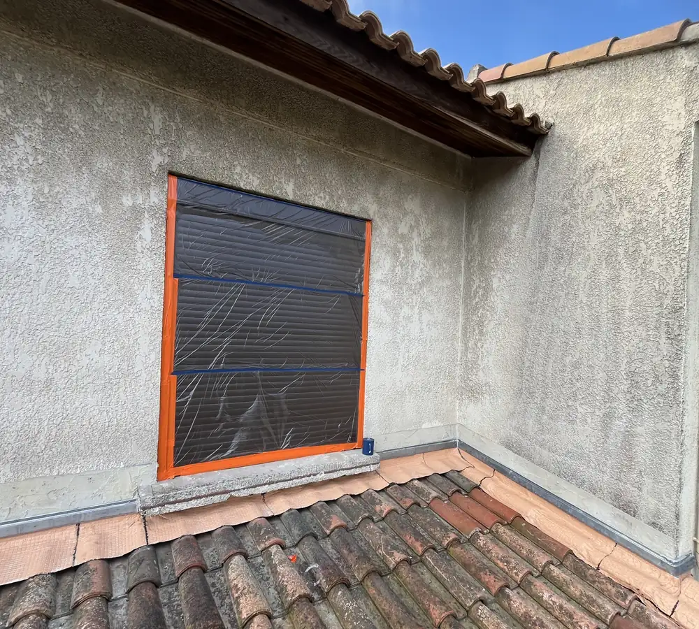 Avant : façade au crépi grisé, fenêtre protégée avant peinture
