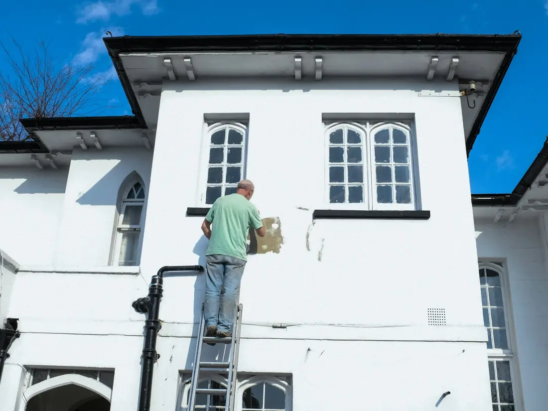 Peintre sur une échelle appliquant une peinture blanche sur la façade d'une maison